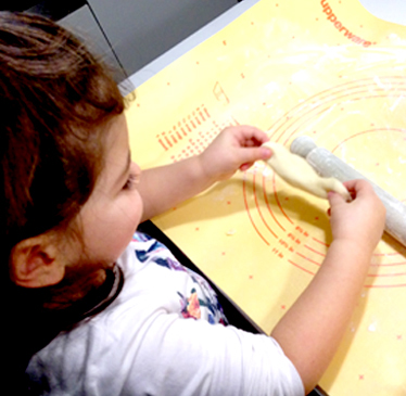 bimba in cucina stende l'impasto per il pane con le mani e il matterello su tappetino tupperware