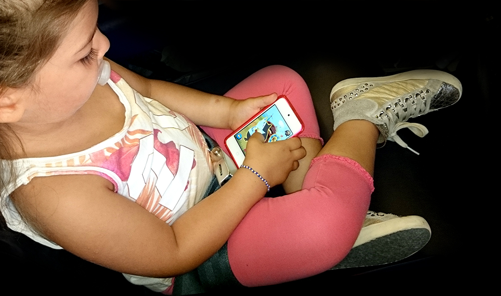 bambina con ciuccio gioca con app puzzle con smartphone in aereo