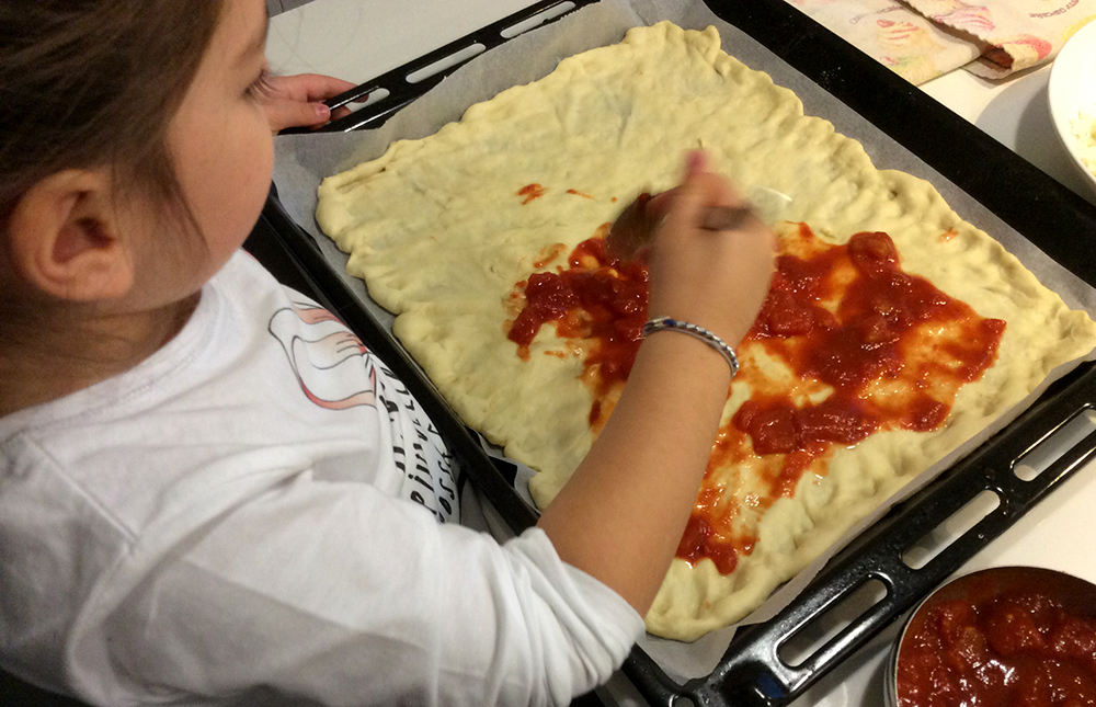 bimba prepara la pizza con la mamma stende il pomodoro sulla pasta nella teglia da forno