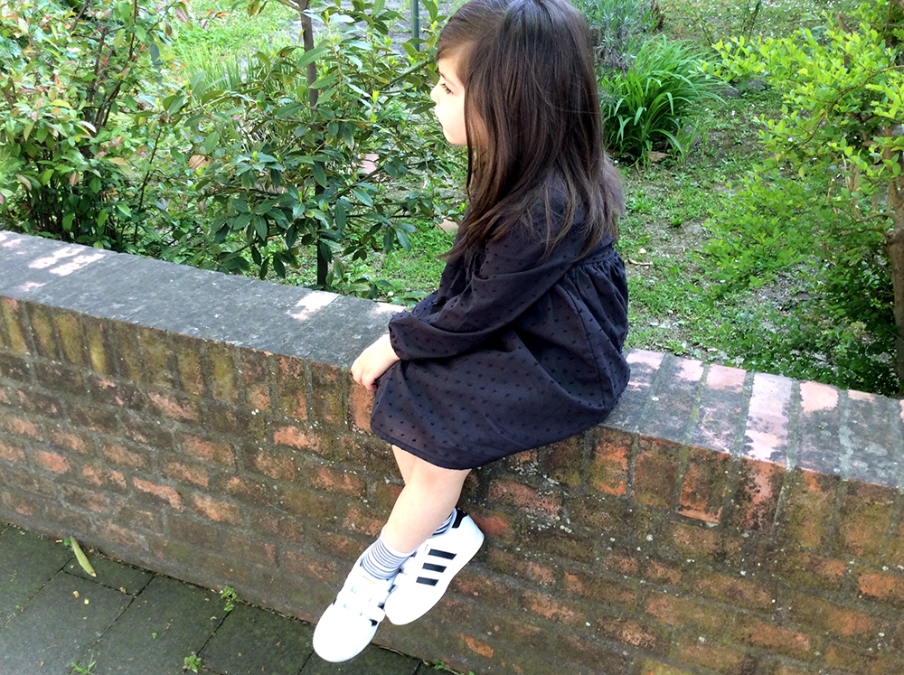 bambina seduta sul muretto con adidas originale superstar e abito tocoto vintage