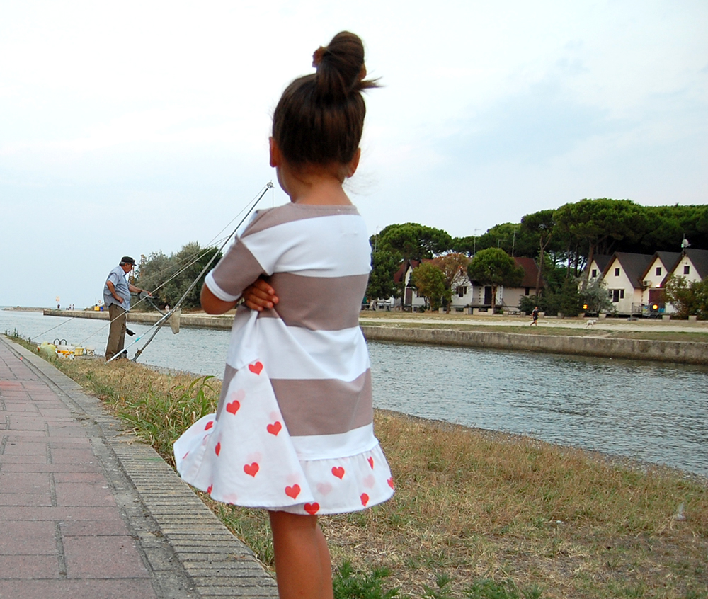 bambina osserva pescatore con abito a righe e cuori rossi